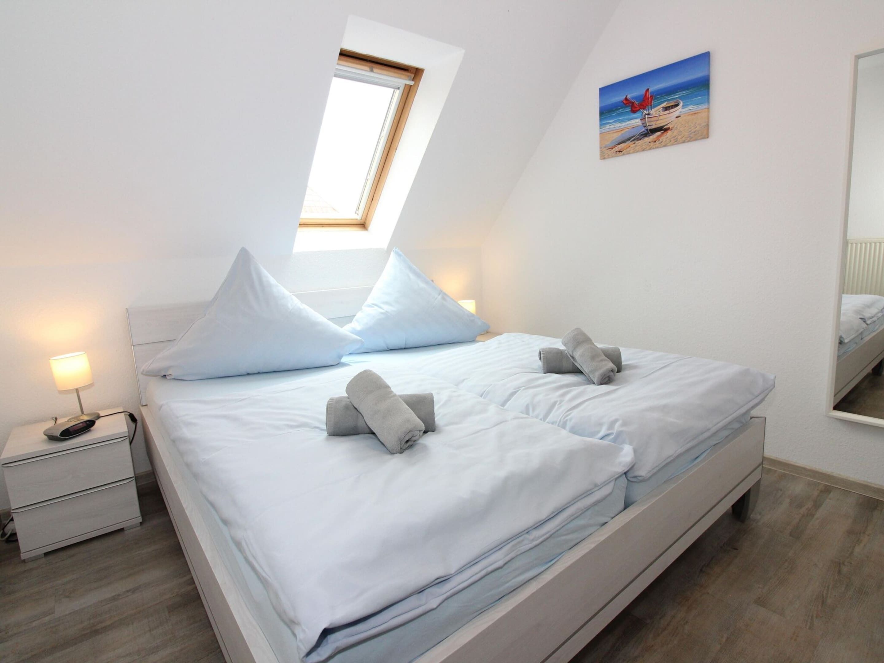 A bedroom with a bed, a nightstand, a lamp, a painting, and a skylight.