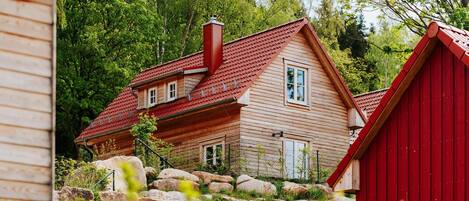 A wooden house with a red roof, surrounded by rocks and trees.