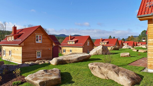 Wooden cabins with red roofs, large rocks, and a clear sky. - Ferienhauser im Schierke Harzresort (Wernigerode)