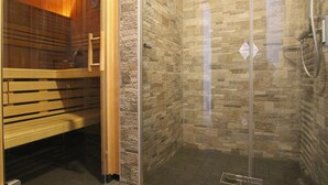 Un baño moderno con ducha de vidrio, banca de madera y paredes de baldosas de piedra.