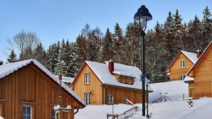 Cabañas de madera con techos nevados y una farola en un paisaje cubierto de nieve.