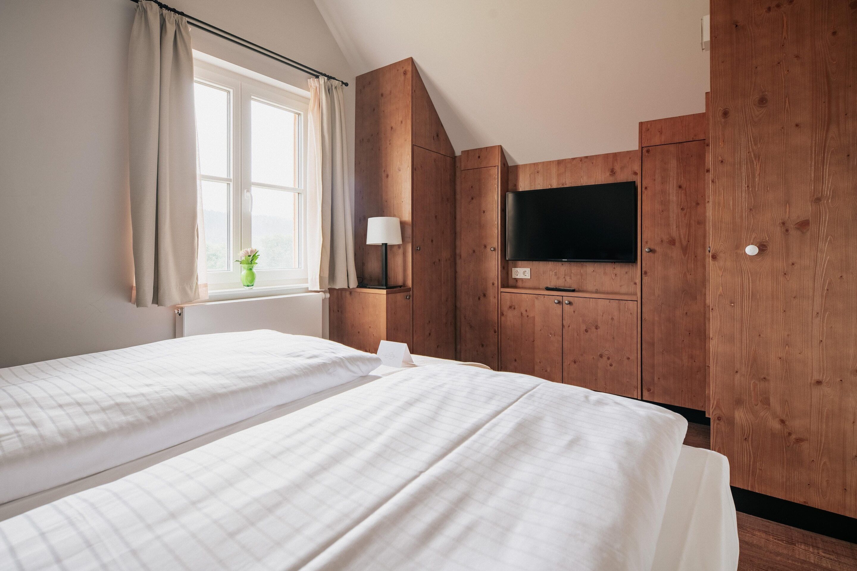 A hotel room with two beds, a TV, wooden paneling, and a window with curtains.