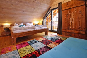 A cozy attic bedroom with a wooden bed, a colorful quilt, and a large window with a deer carving on the wall. - Cottage, Schierke (Wernigerode)