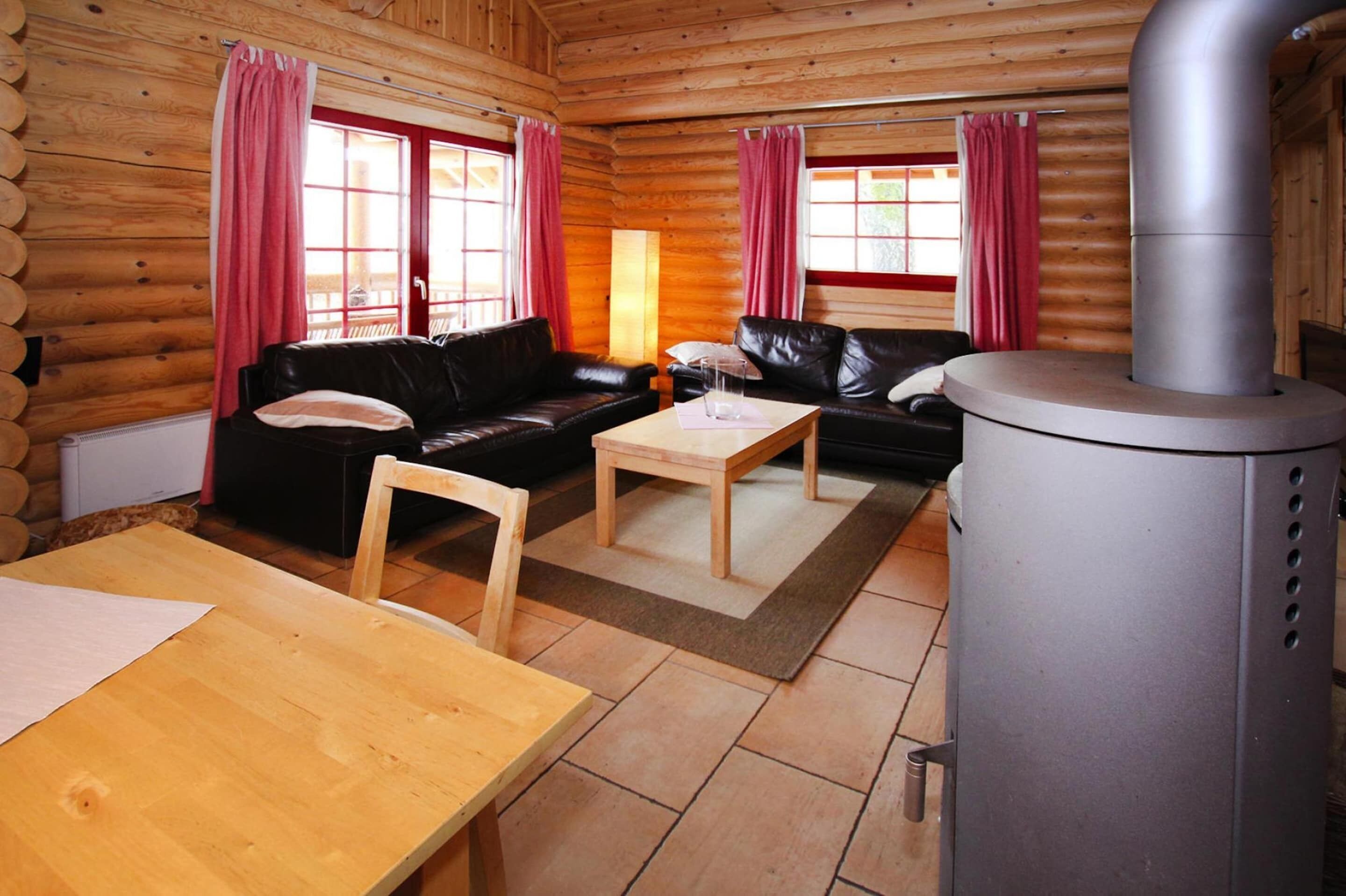 L’intérieur d’un chalet en rondins, avec deux canapés en cuir noir, une table en bois et un poêle à bois.