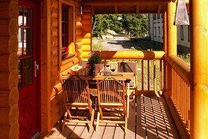 Une cabane en bois avec une véranda, deux chaises en bois, une table et une porte rouge.