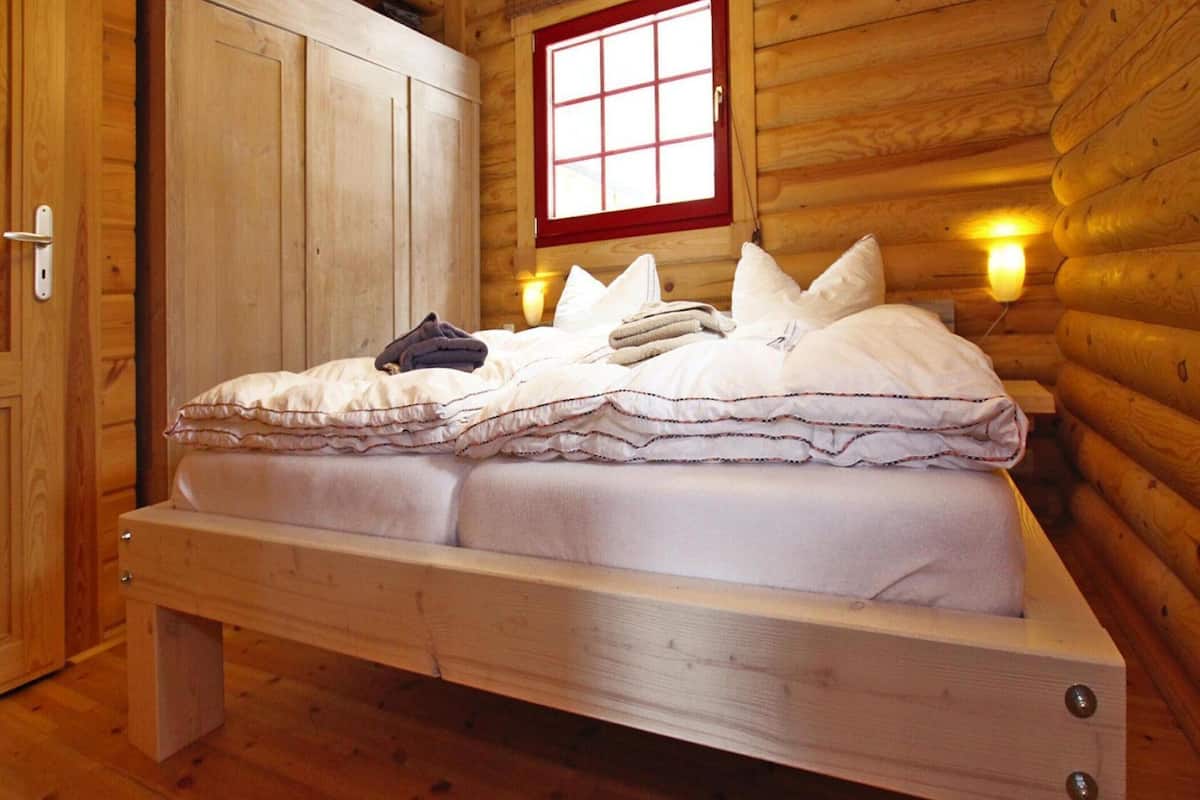 Une pièce de cabane en bois comprenant un lit, une armoire et une fenêtre avec un cadre rouge.