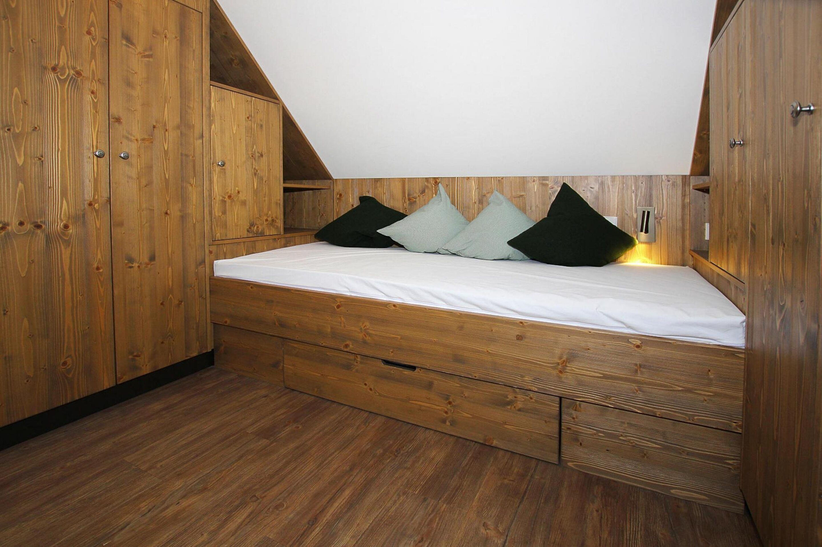 Un dormitorio estilo loft con techo inclinado, piso de madera y muebles empotrados de madera, incluyendo una cama con cajones y un armario.