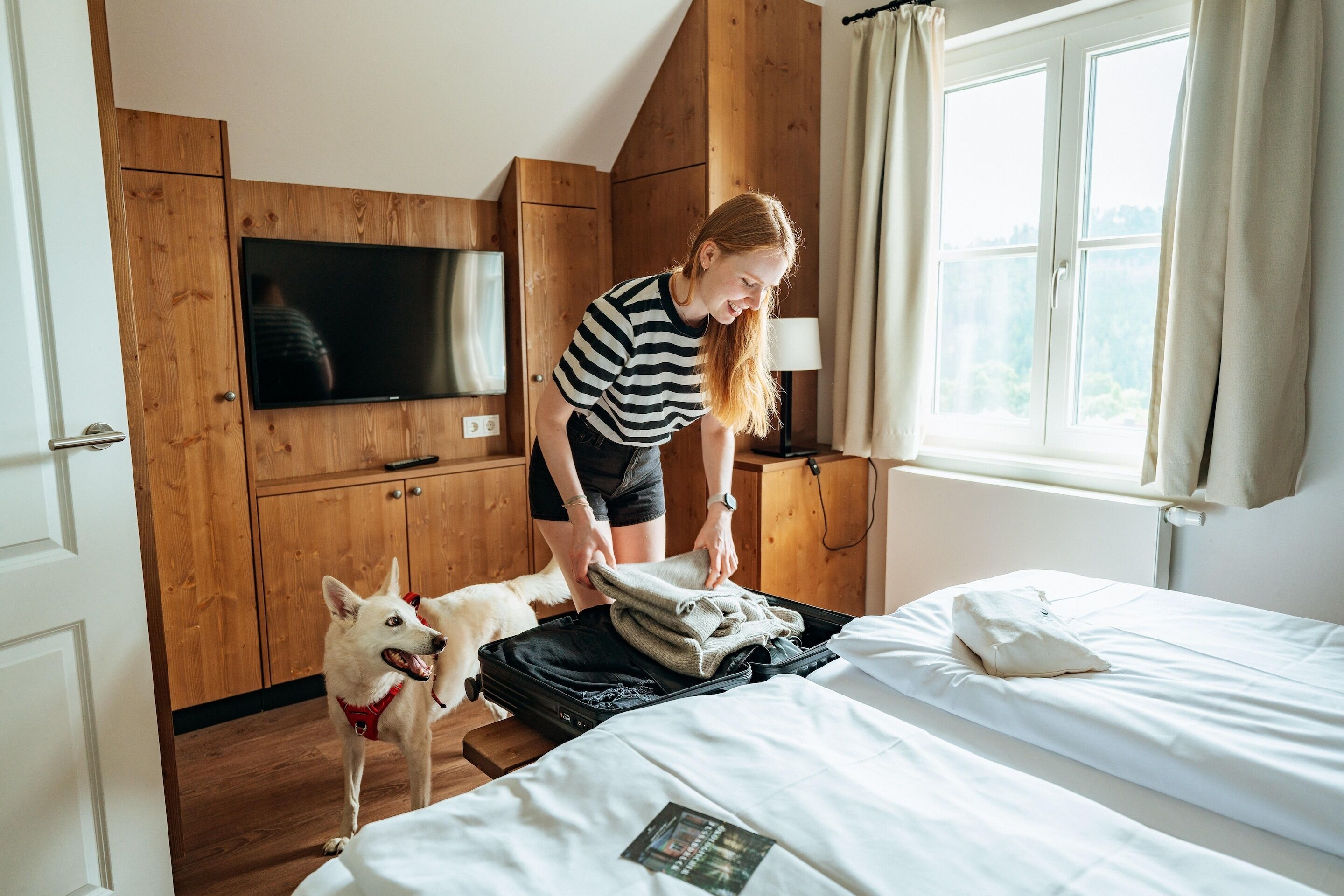 Una habitación con cama, televisor en la pared, armarios de madera y una ventana con cortinas.