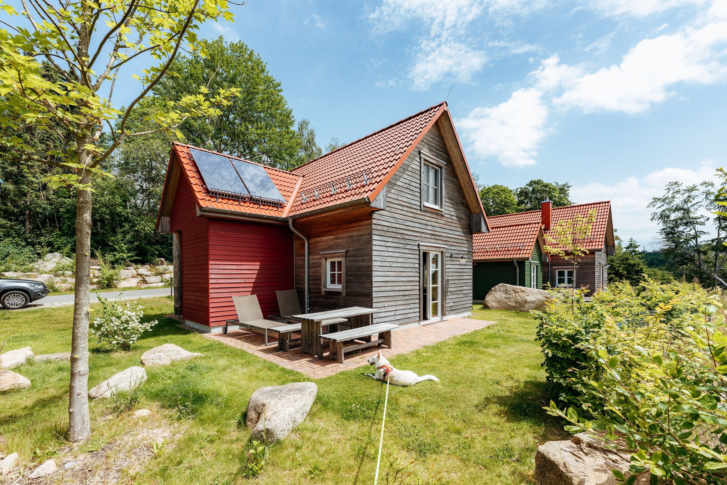 A two-story house with a red and gray exterior, a wooden deck, and a picnic table.