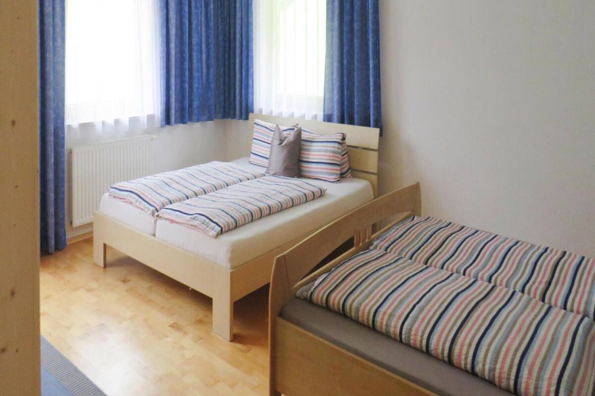 Une chambre avec deux lits simples, un plancher en bois, un radiateur et des rideaux bleus.