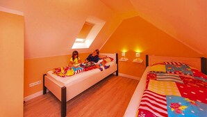 Una camera da letto con soffitto spiovente, una finestra a lucernario, un letto con copripiumino colorato e due comodini con lampade.