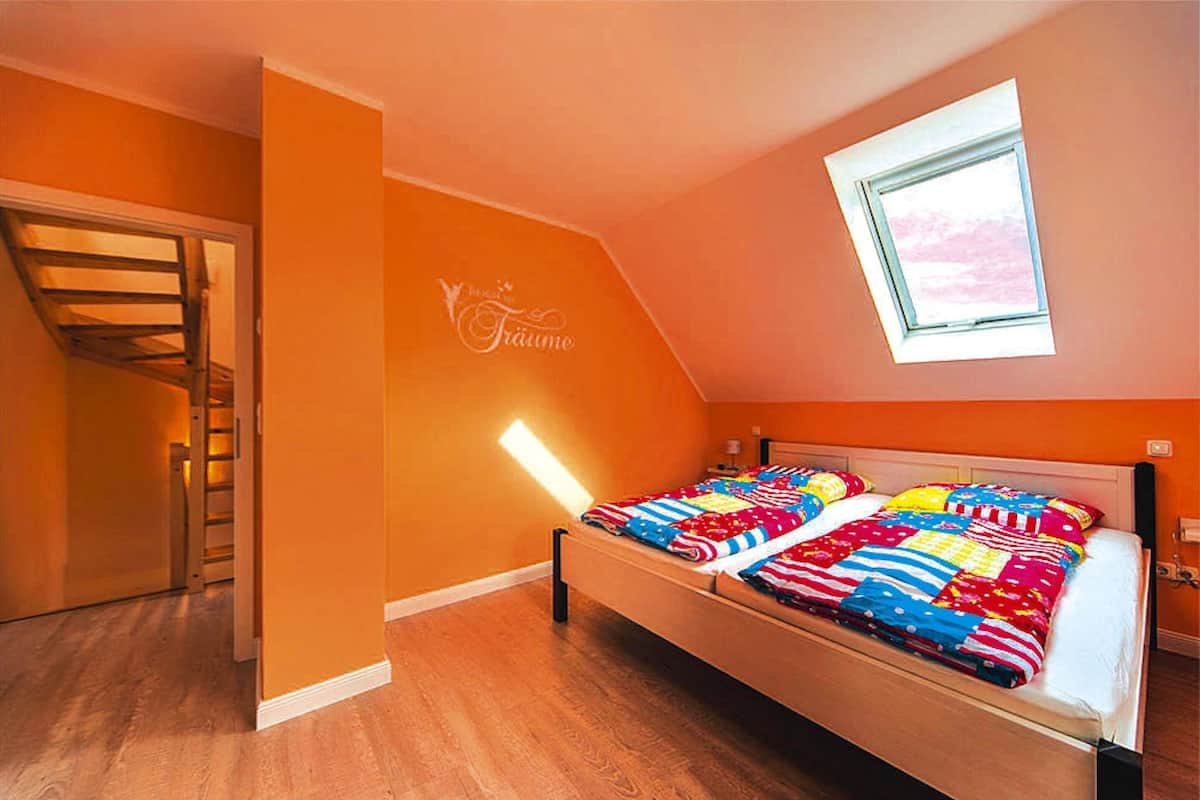 Camera da letto con un letto di legno, pareti arancioni, un lucernario e una scala.