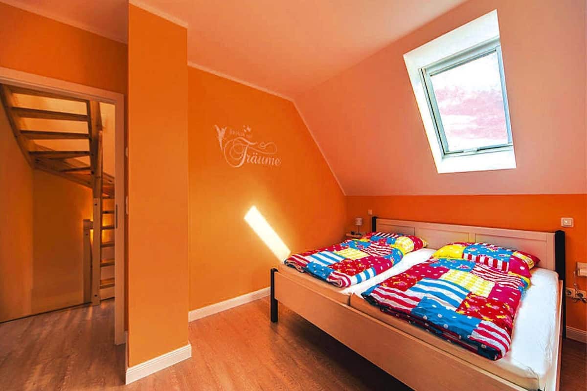 Camera da letto con soffitto spiovente, un lucernario, un letto con biancheria colorata e pavimento in legno.