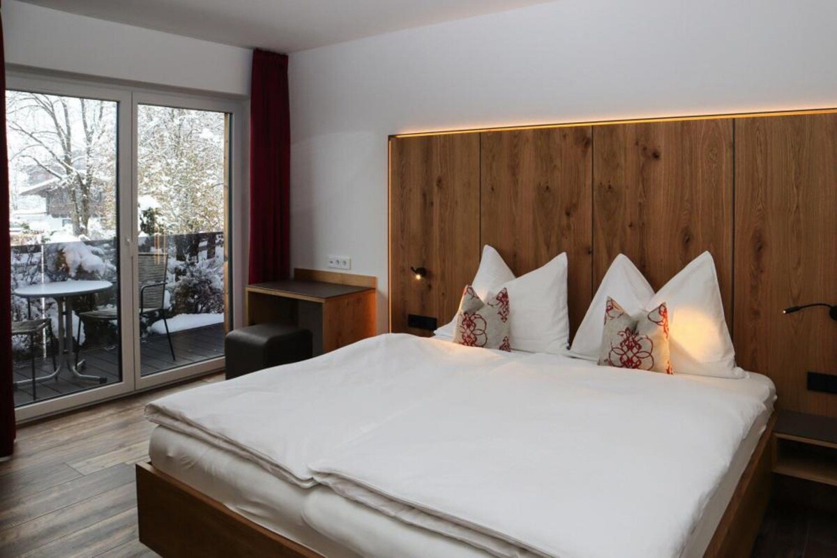 Ein modernes Schlafzimmer mit einem großen Bett, einem Holzkopfende und einer Schiebeglastür zu einem Außenbereich.