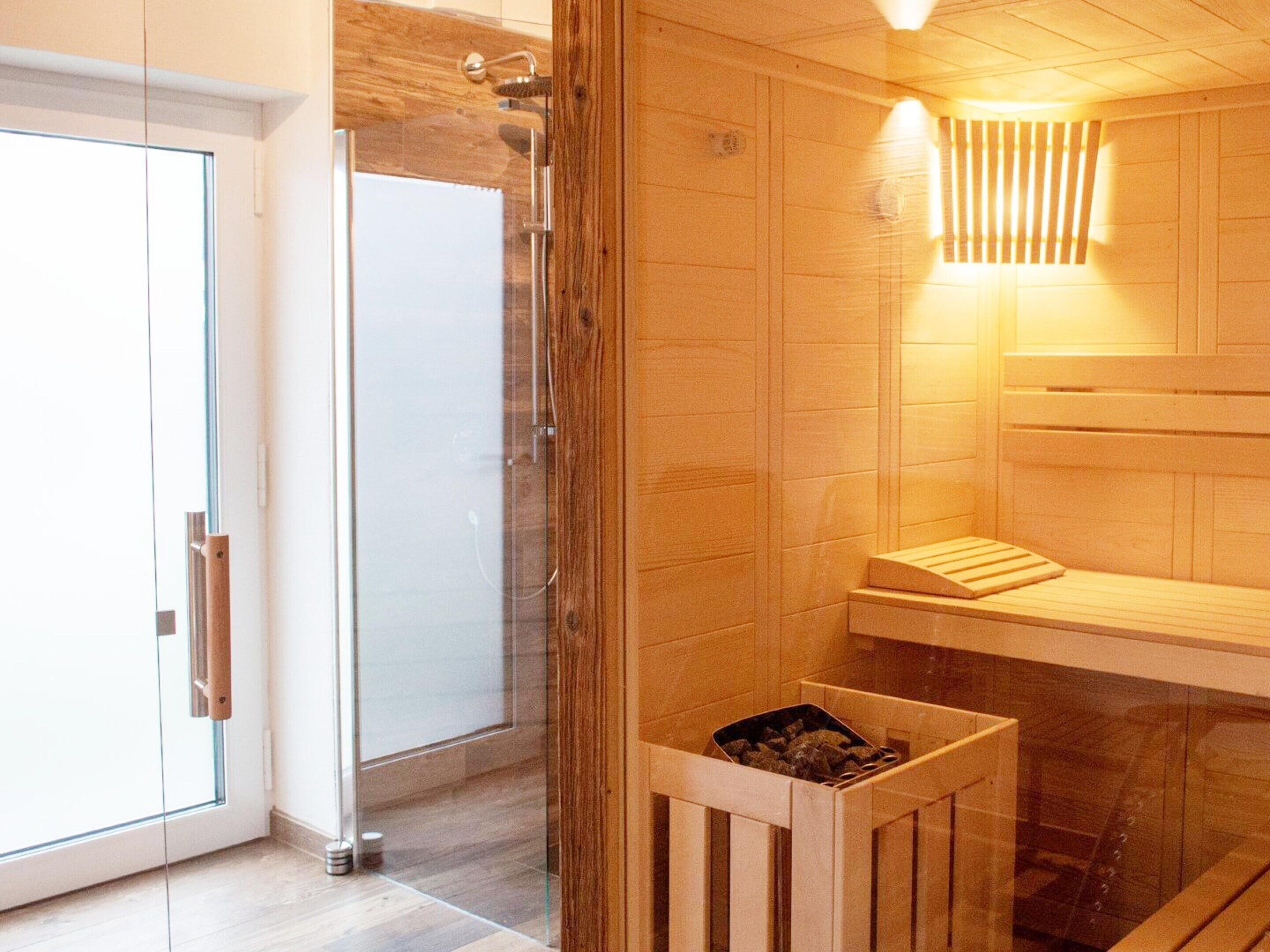 Un sauna doté d’une porte en verre, de bancs en bois et d’un radiateur fixé au mur.