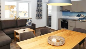 Una sala de estar moderna con un sofá, una mesa de comedor de madera y una cocina con estufa y armarios.