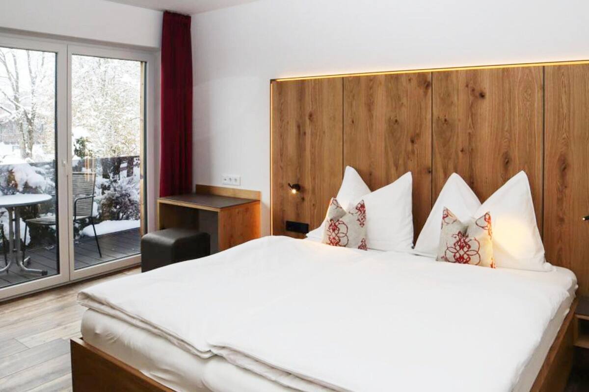 A modern hotel room with a large bed, wooden headboard, and a sliding glass door to a balcony.