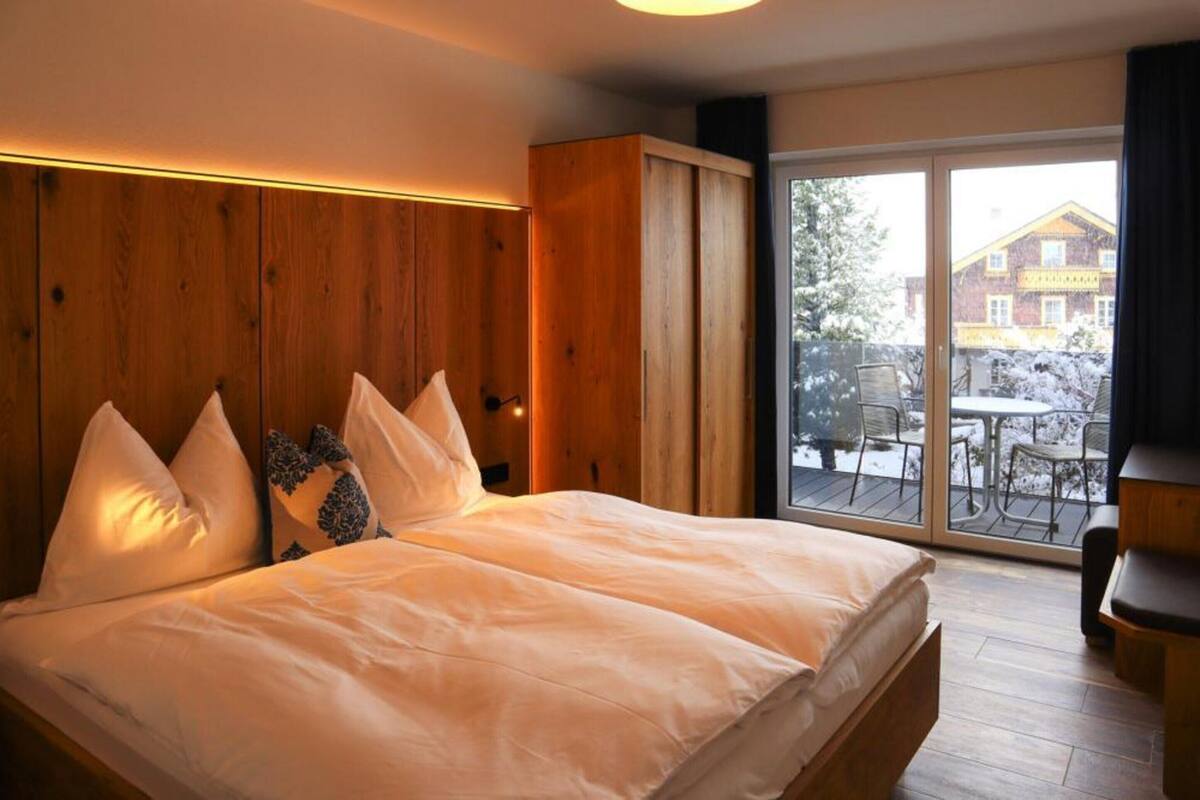 Un dormitorio con una cama grande, cabecera de madera y vistas a un paisaje nevado a través de una puerta corrediza de vidrio.