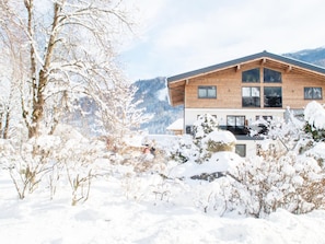 A modern wooden house with large windows and a balcony, surrounded by snow-covered trees and mountains. - Apartment in Bramberg am Wildkogel With Barbecue (Bramberg am Wildkogel)