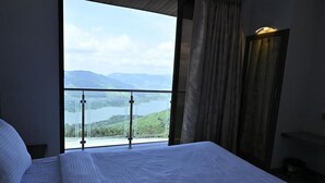 Ein Hotelzimmer mit einem großen Bett, Blick auf einen See und Berge sowie einem Balkon mit Glasgeländer.