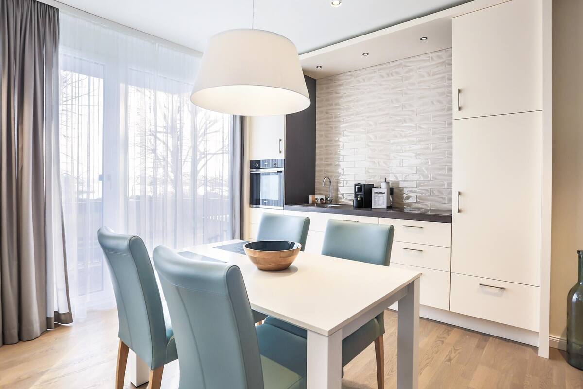 Een moderne keuken met witte kastjes, een wit aanrechtblad en een groot raam met lichte gordijnen.