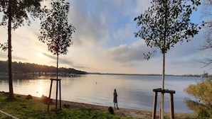 A lakeside view with a person walking along the shore, surrounded by trees and a clear sky. - Apartments in the Maremuritz Yachthafen Resort, Waren an der Muritz (Waren (Müritz))