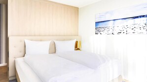 A bedroom with a large bed, a wooden headboard, and a painting of a beach scene. - Apartments in the Maremuritz Yachthafen Resort, Waren an der Muritz (Waren (Müritz))