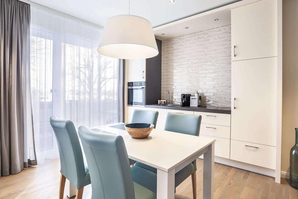 A modern kitchen with white cabinets, a built-in oven, and a large window with sheer curtains.