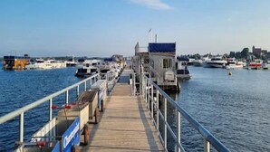A pier with boats docked, a lifeguard tower, and a cityscape in the background. - Apartments in the Maremuritz Yachthafen Resort, Waren an der Muritz (Waren (Müritz))