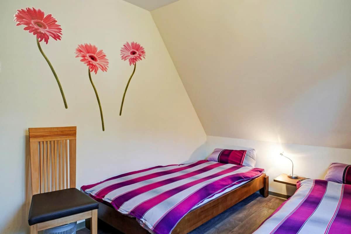 Ein Schlafzimmer mit zwei Betten, einem Holzstuhl und einer Wandlampe.