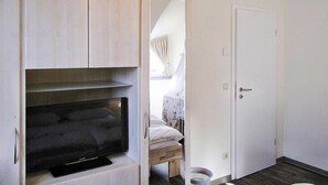 A room with a built-in TV, a door, and a small window with curtains. - Holiday House Nightingale, Glowe (Glowe)