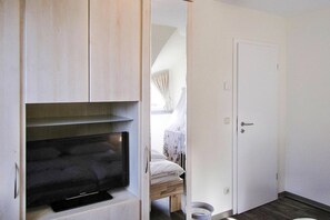 Ein Zimmer mit integriertem Fernseher, einer Tür und einem kleinen Fenster mit Vorhängen.