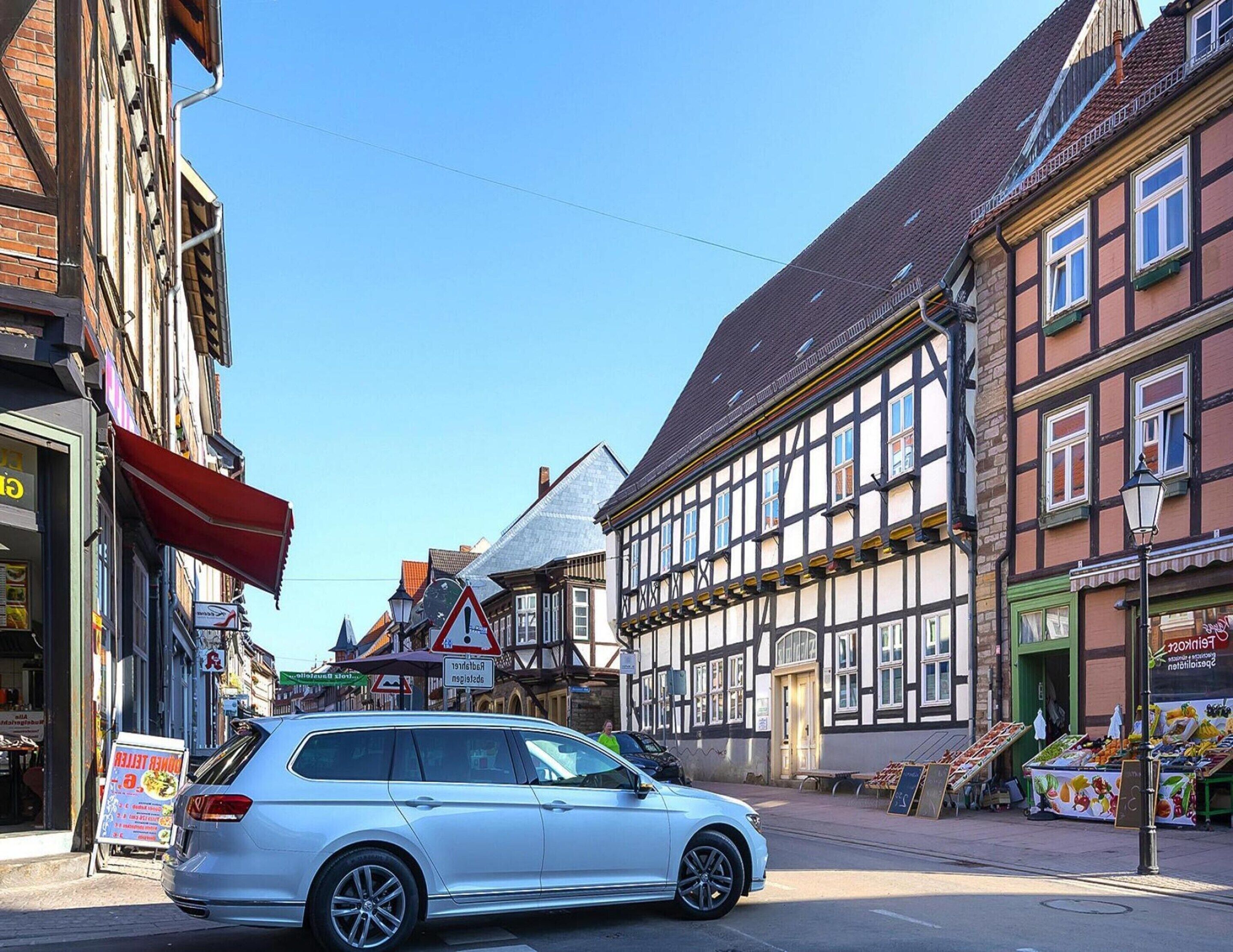 Vista de una calle con edificios tradicionales de entramado de madera, un coche aparcado a un lado y un puesto de frutas a la derecha.