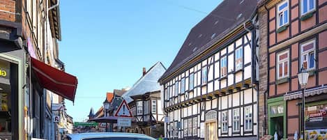A street view with traditional half-timbered buildings, a car parked on the side, and a fruit stand on the right.