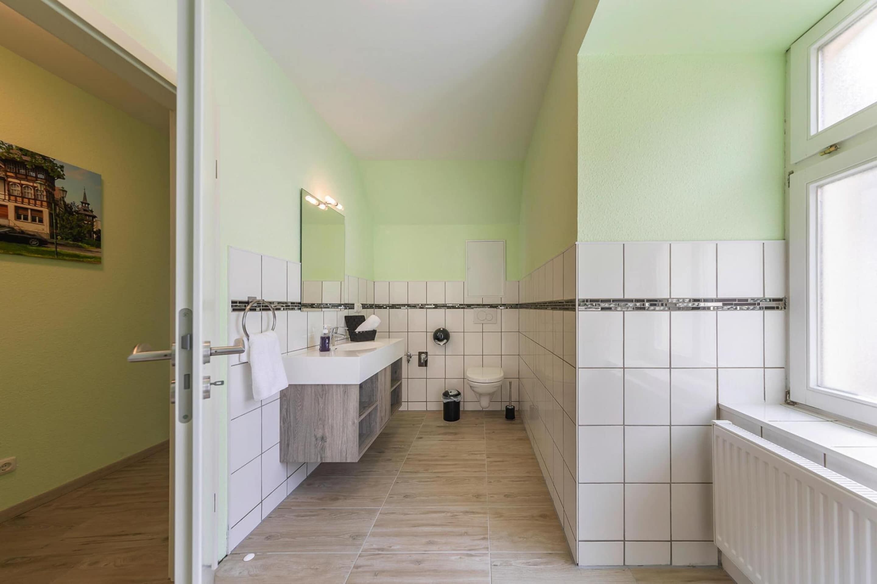 A narrow bathroom with a white sink, mirror, and toilet.