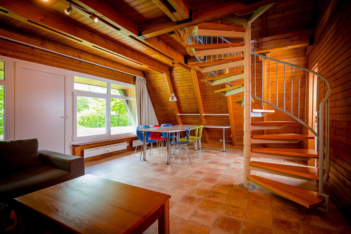 Een houten interieur met een trap, een eethoek en een bank.