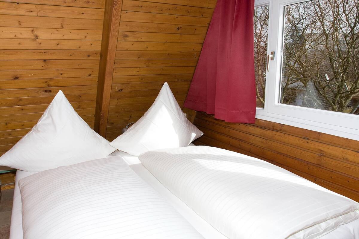 Une pièce de cabane en bois comprenant un lit, des oreillers et une fenêtre avec un rideau rouge.