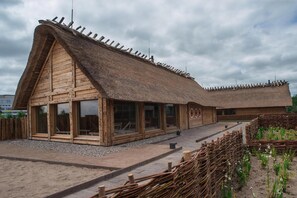 Ein hölzernes Gebäude mit Strohdach, großen Fenstern und einem Kiesweg.
