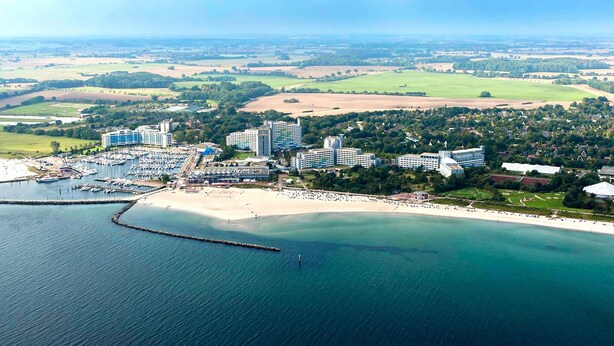 An aerial view of a coastal hotel with multiple buildings, a marina, and a beach. - Ferienhaus im Ostseeresort Dampland in Perfekter Lage (Damp)