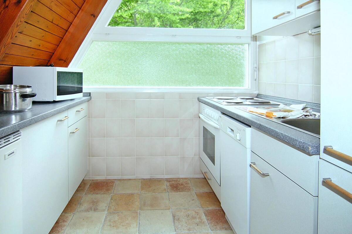 Une cuisine compacte avec des meubles blancs, un four à micro-ondes, une cuisinière et une fenêtre donnant sur un espace verdoyant.
