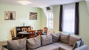 A living room with a sectional sofa, dining table, chairs, and artwork on the walls. - Apartment Schlossblick, Wernigerode (Wernigerode)