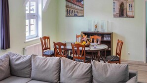 A cozy living room with a sofa, dining table, and chairs. There are paintings on the walls and a window with curtains. - Apartment Schlossblick, Wernigerode (Wernigerode)
