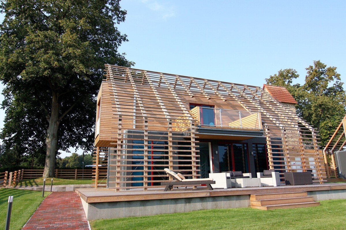 A modern house with a sloped roof, large windows, and a wooden deck with outdoor furniture.