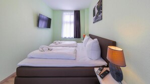 Een hotelkamer met een bed, een tv aan de muur, een raam met gordijnen, een bedlampje en een afstandsbediening op het nachtkastje.