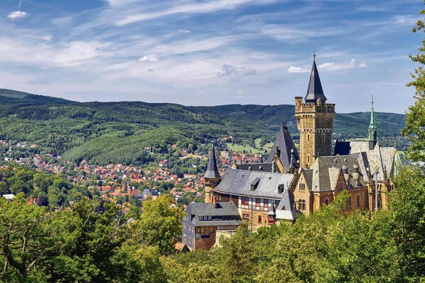 A historic building with a prominent tower and spires, surrounded by lush green hills and a town below.