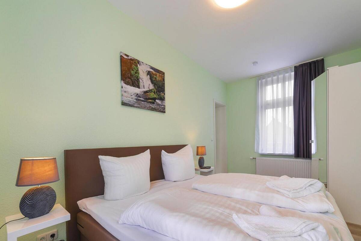 A neatly made bed with white linens, a brown headboard, and a wall-mounted painting of a waterfall.