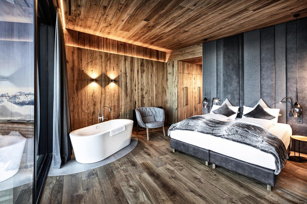 A modern bedroom with a large bed, a bathtub, and a chair.