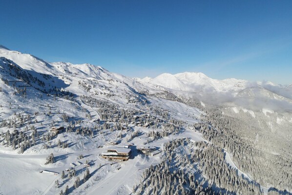 A snow-covered mountain landscape with a ski resort, including buildings and ski trails.