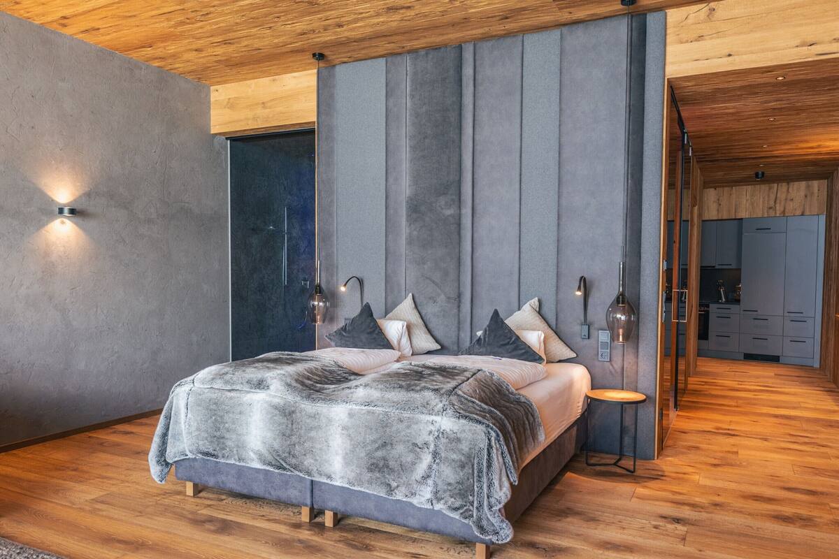 A modern bedroom with a large bed, wooden flooring, and a built-in wardrobe.