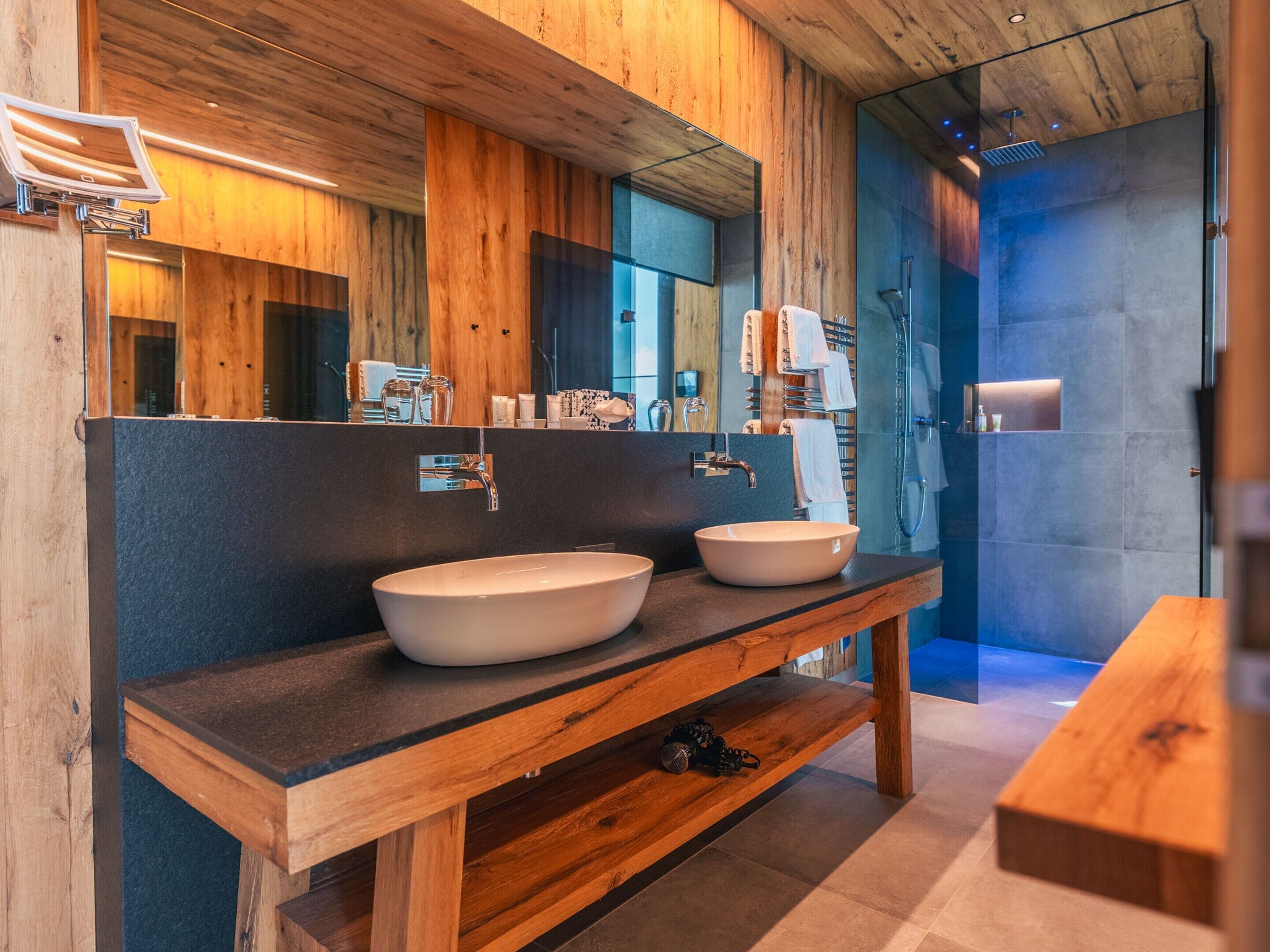 Un baño moderno con detalles de madera, un espejo grande y una ducha a ras de suelo.